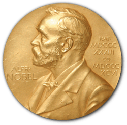 A golden medallion with an embossed image of a bearded man facing left in profile. To the left of the man is the text "ALFR•" then "NOBEL", and on the right, the text (smaller) "NAT•" then "MDCCCXXXIII" above, followed by (smaller) "OB•" then "MDCCCXCVI" below.