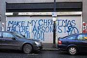 Graffiti on a metal shutter door reads "Make my Christmas. Jail the arsonists. Shame on you."