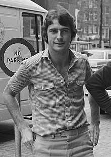 Black and white photo of young white man with dark wavy hair wearing an open-necked shirt