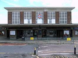 A brown-bricked building with a rectangular, black sign reading "OAKWOOD STATION" in white letters all under a light blue sky
