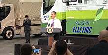 A smiling Barack Obama at a podium in front of an electric truck