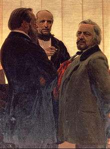 Three men standing together&nbsp;– two men with beards, the one on the right with grey hair, flanking a third man watching them intently