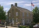 A two-story limestone building with two chimneys and a United States flag flying in front