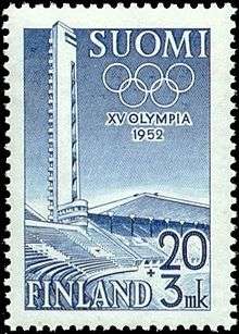 A soild blue background is intruded on its left side by a structure, shaded in white, representing the tower and stand of the Helsinki Olympic Stadium. The Olympic rings, also white, lie at the top of the blue background, partly obscured by the stadium's tower. The word "1952" is written in white in the middle of the blue background, while "XV Olympia Helsinki" is written in blue, beneath the image.