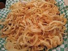 Crispy, golden fried onions sit upon a green and white checkered paper.