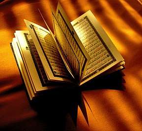 A paper Quran opened halfwise on top of a brown cloth