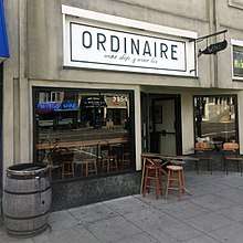 The exterior of Ordinaire. There is a barrel, a small table with stools, and a small sign with the word "wine" on it in the shape of a whale