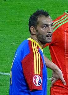 A man with dark hair wearing a red, blue and yellow jersey.