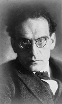 head and shoulder image of man with dark hair and spectacles, glaring towards the camera