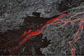 Aerial photograph of volcanic rock, with black cold lava split by a bright river of red lava