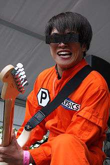 A picture of a man in an orange jumpsuit, rectangular sunglasses, playing a guitar.