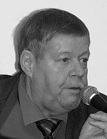 Sepia photo: Face shot of Arto Paasilinna, speaking in a microphone.