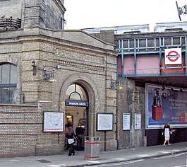 A beige-bricked building with a rectangular, dark blue sign reading "PARSONS GREEN" in white letters all under a light blue sky with white clouds