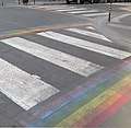 Zebra crossing with rainbow stripes running perpendiculary along its sides.