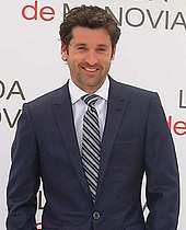 Patrick Dempsey smiling, wearing a navy blue suit.