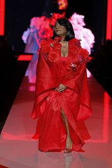 A woman in a red dress walks down a catwalk