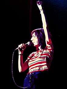 A color photograph of Patti Smith on stage with a microphone