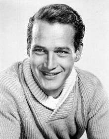 Black-and-white photo of Paul Newman in 1958—a 33-year-old man with light eyes, broad shoulders, smooth dark hair brushed to the side and a thin nose, wearing a long light-colored shirt.