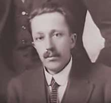 Black and white photograph of a young man with a moustache, dressed in a jacket and tie