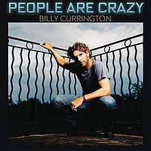 The cover has the artist wearing a blue t-shirt and jeans combination, crouching and having his right arm hold next to a black art deco fence. The song title is set above the image, colored in neon blue, with the artist's name below it in white.