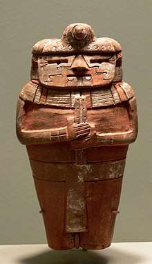 Squat, reddish ceramic figurine of a person holding a flute
