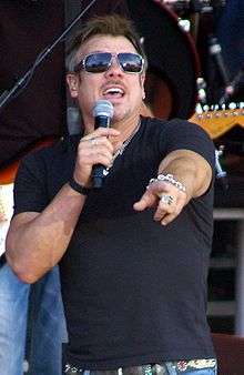 A man wearing dark glasses and a dark T-shirt singing into a microphone