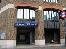 A brown-bricked building with a rectangular, dark blue sign reading "PIMLICO STATION" in white letters and a black sign reading "UNDERGROUND"