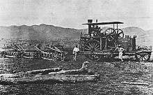 A steam-tractor in a field. Three men stand beside the machine.