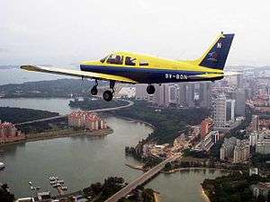 A Piper Warrior II in the SYFC livery flying over central Singapore