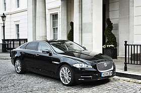 A black Jaguar XJ LWB Sentinel parked stationary on a cobbled street in front of a white building.