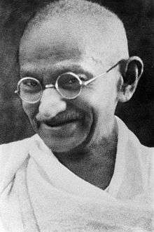 The face of Gandhi in old age – smiling, wearing glasses, and with a white sash over his right shoulder