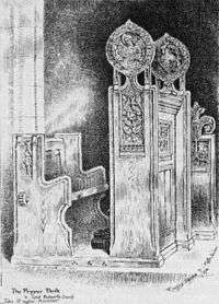A black and white image showing a church seat on the left and the carved side of the prayer desk in front of it