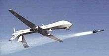 A General Atomics MQ-1 Predator drone, having the appearance of a small unmanned mini-plane, firing a missile.