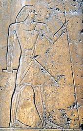 Relief on stone showing the profile of a man wearing a linen robe and holding a staff.