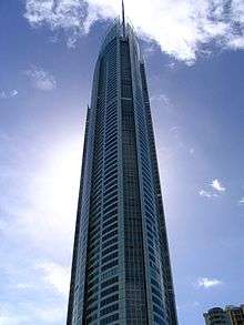 The tall, thin building rises into a blue sky flecked with a few clouds.