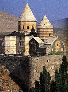 Stone church in the mountains with two massive towers topped by a conical roof