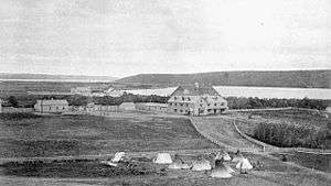 Exterior view of Qu'Appelle Indian Industrial School in Lebret, District of Assiniboia, ca. 1885. Surrounding land and tents are visible in the foreground.