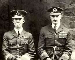 Half portrait of two men in dark-coloured military uniforms with peaked caps