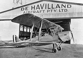 Biplane on tarmac in front of hanger marked "De Havilland Aircraft Pty Ltd"