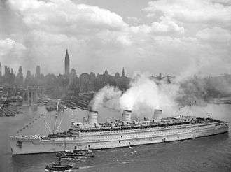 Black and white photograph showing the port side of the RMS Queen Mary entering New York Harbor on 20 June 1945 being accompanied by two small tug boats