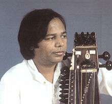 Narayan looks to the side with a sarangi held close to his body.