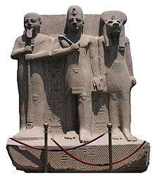 Statue of a man with a crown standing between a man holding a staff and a woman with the head of a lioness
