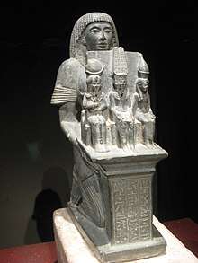 Statue of a man seated and holding three smaller statues of gods.