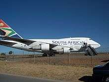 A Boeing 747SP, a shortened Boeing 747-100. The aircraft's engines feature prominently, as a mobile stairway is placed next to one of its doors under the "N" in South African.