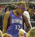 Young woman with braided hair dyed light brown wearing a purple headband and purple jersey standing in a huddle
