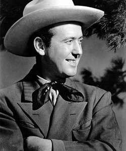 A man wearing a light-coloured cowboy hat, neckerchief and dark jacket