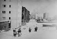Four Finnish soldiers, with their backs shown, are retreating to the demarcation line after the ceasefire came into effect. The city of Vyborg looks empty and smoke is rising in the background.