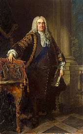 In a full-length portrait, an overweight middle-aged man stands, legs slightly apart, with his right hand resting on the top of a coat of arms, leant on the top of an ornate table.  In his left hand he holds a large white document.  He is dressed in expensive 18th-century clothing, with a blue sash over his left shoulder, and a long grey wig.  Behind him, a large pale column of stone rises from a tiled floor.  A balustrade connects to the column, and a small green plant is visible.