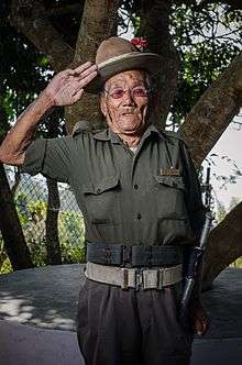 A Gurkha veteran in traditional uniform stands to attention and salutes.