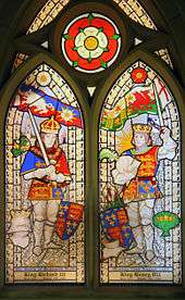 Two men in armour stand opposite each other. They wear crowns and hold swords in their hands. Above the man on the left is a flag of a white boar and a white rose. Above the man on the right is a flag of a red dragon and a red rose. Above and between the two roses is a white rose superimposed on a red rose.